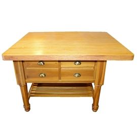 Maple Butcher Block Kitchen Island: A kitchen island with a maple butcher block top. The island features four drawers with brushed nickel pulls. It is supported by four thick turned legs with a lower storage shelf. The top extends over on one side enable room for seating. The piece is unmarked.