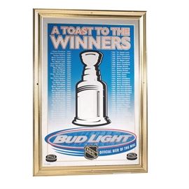 Bud Light Bar Mirror Celebrating NHL Winners: A Bud Light bar mirror celebrating the Stanley Cup winners. This mirror is printed with a list of Stanley Cup winners from 1927 through 1998, and is marked “A Toast to the Winners” to the top, with Bud Light branding towards the bottom. The mirror is housed in a gold tone composite frame and has a pair of D-rings affixed to the verso.