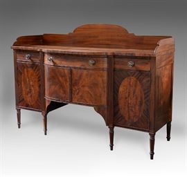 New England Period Sheraton flame mahogany sideboard with a shaped backsplash and bowed center section containing a single drawer over a double door cabinet. The center is flanked with single drawers over cabinets with oval inlaid panels. Fluted pilasters separate the sections and the board is raised on turned legs; 53.5"H x 72"W x 22.75"D
Condition
Very good: wear commensurate with age and use, top center board possibly replaced; minor veneer loss mainly to the front edges and loss of cockbeading with splits to veneer inlays.
Starting Bid
$200.00