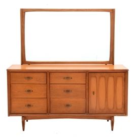 Mid Century "Mainline" Dresser With Mirror by Hooker: A mid century Hooker Mainline dresser with mirror in light walnut finish. The dresser case features a rectangular top with six exterior drawers and a single door, opening to three interior drawers, and standing on a tapered leg base. Marked to inside drawer with maker’s burn mark.