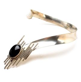 Aaron Rubinstein Signed Modernist Sterling and Onyx Necklace: An Aaron Rubinstein signed Modernist sterling collar necklace. This handcrafted piece is formed as a wide collar necklace offering a dramatic centerpiece of a large oval black onyx cabochon set against a Brutalist-style frame composed of linear tube segments. It bears an etched signature “Aaron Rubinstein, sterling w/black onyx” and is dated 12/26/91. Mr. Rubinstein was born in Poland in 1928, living in Israel and the United States where he studied sculpture and jewelry at the Minneapolis Institute of Art before settling in Cincinnati to open his own business as a contemporary jewelry designer. The total weight of this piece, inclusive of all materials, is 3.105 ozt.