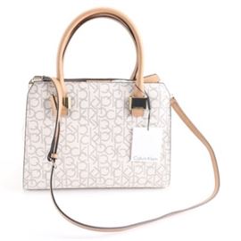 Calvin Klein Monogram Shoulder Bag: A Calvin Klein Monogram shoulder bag. This dual-handled bag showcases a white exterior with a CK pattern. It also includes a tan, adjustable shoulder strap. It is labeled by the manufacturer.