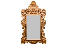 Oversize Ornate Gold Tone Wall Mirror: An ornate oversized gold-tone wall mirror. The rectangular mirror is presented in a gilt faux wood frame depicting a face in the pediment surrounded by scrolling acanthus which flows down the sides and along the bottom.