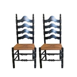Pair of Black Ladder Back Hitchcock Style Chairs: A pair of black ladder back Hitchcock style chairs. They have black painted wooden frames, with arched ladder backs and turned stiles, front legs, and front stretchers, accented with gold tone throughout and with a harvest theme motif to the top rail. They have rush woven seats.