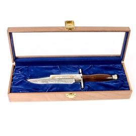 Harley-Davidson Black Hills Commemorative Knife by Buck: A Harley-Davidson Black Hills commemorative knife by Buck. Featured here is a wood handled knife with a metal blade decorated with a depiction of the Black Hills of South Dakota. The blade reads “Black Hills Commemorative” on one side and has a “Fiftieth Anniversary, 1990” inscription on the reverse. It is numbered 0971/3000 and branded “Buck Custom U.S.A.” The knife comes with a certificate of authenticity and is displayed in a wooden box with blue felt lining and a clear glass lid.