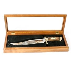 100th Anniversary Harley-Davidson Knife: A 100th anniversary Harley-Davidson knife. Featured here is a wood handled knife with a metal blade decorated with a group of men on one side of the blade. The blade guard reads “100 Years of Great Motorcycles” and “1541” on the top of the handle. Inlaid into the wooden handle is the Harley-Davidson insignia. The knife comes displayed in a wooden box with black felt lining and a clear glass lid dated 2003.
