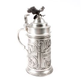 Harley-Davidson Pewter Stein by GERZ "The Most Desirable Motorcycle": A Harley-Davidson pewter stein by GERZ The Most Desirable Motorcycle. Featured here is a solid pewter lidded stein with an eagle perched on the lid. Around the outside of the base are depictions of motorcycle scenes and a Harley-Davidson logo. Beneath the logo, the stein reads “The Most Desirable Motorcycle”. The bottom of the stein is marked “Harley-Davidson, 1989, Limited Edition 650 of 2000, GERZ Made in W. Germany”. A certificate of authenticity is included.