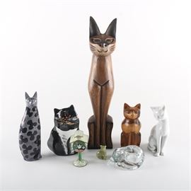 Cat Figurine Collection: A collection of cat figurines. Includes a glass cat votive, a metal cat themed miniature “mail box,” a small agate cat, a tall cat with black and grey pattern, a black and white cat vase with grumpy face, tall wooden cat, small wooden cat, and white ceramic cat.
