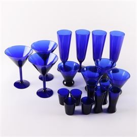 Cobalt Blue Glassware: A selection of cobalt blue glassware. Includes four stemless cocktail glasses, four tall shot glasses, three martini glasses, four short shot glasses, and four pilsner glasses. The pieces are unmarked.