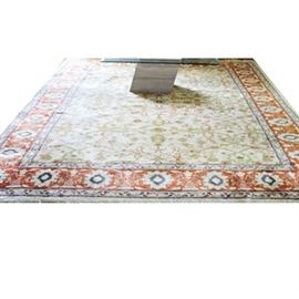 Hand-Knotted Indian Area Rug: A hand-knotted Indian area rug. This Super Bana rug is constructed from 100% virgin wool pile. The field has a pattern of palmettes and stylized herati in colors of taupe, scarlet and green on a white field. The main border features a repeating Shah Abbasi palmette and floral pattern in pale blue, steel grey and indigo over a red field. It has overcast edges and a natural, plaited cotton warp fringe to either end. Tagged to underside.