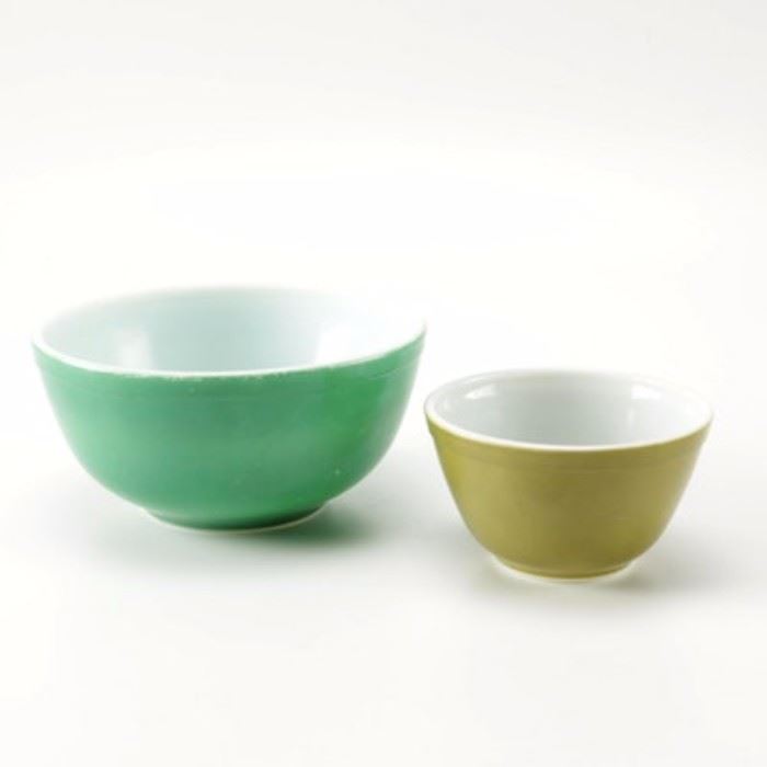 Vintage Pyrex Green Glass Mixing Bowls: A pairing of glass mixing bowls by Pyrex. This selection includes a large bowl with a green exterior and white translucent center and a smaller bowl in the Verde pattern with a pea green exterior and white translucent center. Each is embossed “Pyrex, Made in USA” to the underside.