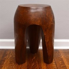 Contemporary Solid Wood Accent Table: A contemporary solid wood accent table. This piece is circular, with a drum appearance and a mottled finish. It stands on three legs, with arched negative space between them. It is unmarked.