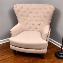 Jofran "Conner" Fanback Armchair: A Jofran “Conner” fanback armchair. This chair features a tufted back, narrow arms, and a cushioned seat. It is upholstered in beige fabric with brass nailhead trim and rests upon tapered wooden legs. The piece is tagged to the underside.
