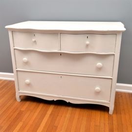 Vintage Serpentine Front Dresser: A vintage serpentine front dresser. This piece has a distressed white finish, with an undulating serpentine front to the drawer fronts, and the tops front edge. It offers two half-length drawers at the top and two full-length drawers below, all with dovetail joinery and wooden knobs. It has a scalloped apron and stands on square feet.