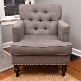 Permaisuri Grey Upholstered Armchair: A Permaisuri armchair. This chair features a squared, tufted back and seat. It has straight arms and is upholstered in gray fabric with silver tone nailhead trim to the arms and apron. The piece rests upon turned wooden legs with a black-painted finish and is tagged to the underside.