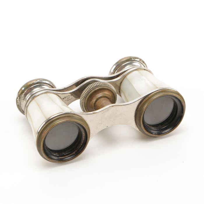 Chevalier of Paris Mother of Pearl Opera Glasses: A pair of mother of pearl opera glasses by Chevalier of Paris. These opera glasses or binoculars have mother of pearl paneling on both barrels, in a silver-tone frame with a focusing knob at the center. Both eyepieces are marked “Chevalier Paris,” and the frame is marked “Made in France.”