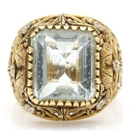 18K Yellow Gold 7.70 CT Aquamarine Foliate Ring: An 18K yellow gold 7.70 ct aquamarine foliate ring. This ring features a center prong set aquamarine within a pierced gallery of textured ivy leaves, beveled scroll work, and round floral accents.