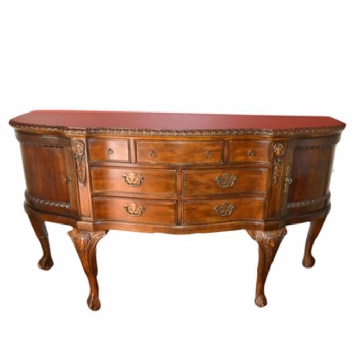 Chippendale Style Buffet: A Chippendale style buffet. This piece has a walnut finish, with brass-toned batwing pulls, shield shaped drop pulls, and faux keys with escutcheons. The serpentine front features seven drawers in various sizes to the center, flanked by two curved recessed panel doors to the sides. The piece rises on four carved cabriole legs with ball and claw feet.