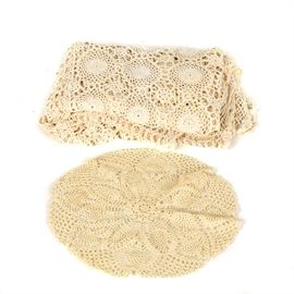 Crocheted Tablecloth and Doily: A pair of crocheted table settings. This includes a tablecloth and doily. They are made of a beige yarn with floral accents.