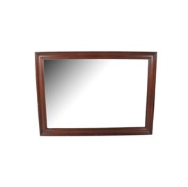 Rectangular Wood Framed Wall Mirror: A rectangular wood framed wall mirror. The mirror has a beveled edge and is surrounded by a dark stained and finished wood frame with beveled edges. The mirror has a wood backing and a wire for hanging.