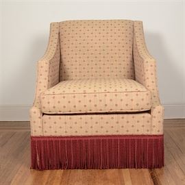 Lounge Chair by The Charles Stewart Company: A lounge chair by The Charles Stewart Company. This item features a rectangular back with short, sloped arms which originate at its crest. Its seat cushion is removable and sits above a red-tasseled skirt. It is marked by the maker under the seat.