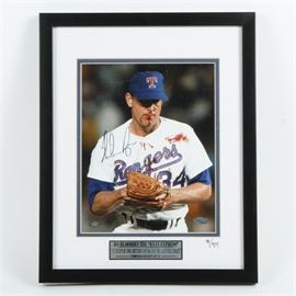 Limited Edition Signed Photo of Nolan Ryan With Bloody Lip: A signed photo of Nolan Ryan. This photo depicts Nolan Ryan, former pitcher for the Texas Rangers, holding his fist in his glove and licking his lip which is smeared with blood. The photo is signed to the center and is presented behind a white and blue mat, under glass in a black wood frame with a wire mount to the verso. There is a label underneath the photo that reads “Bo Bloodies the ‘Ryan Express’ ‘It helps if the hitter thinks you’re a little crazy’ limited edition of 34” and the mat is numbered 9/34 at the lower right. The back of the frame features a certificate of authenticity from Steiner Sports Memorabilia.