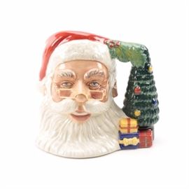 Royal Doulton Santa Claus Ceramic Mug: A Royal Doulton Santa Claus ceramic mug. This Royal Doulton mug displays a hand-painted Santa Claus visage with removable glasses and a handle made of a Christmas tree and presents. The piece is marked to the underside “Royal Doulton Santa Claus D7123”.