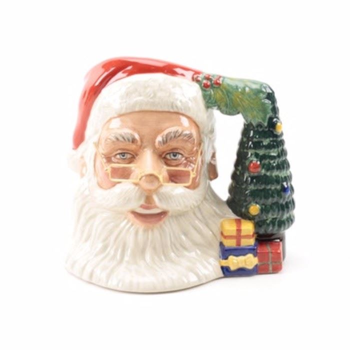 Royal Doulton Santa Claus Ceramic Mug: A Royal Doulton Santa Claus ceramic mug. This Royal Doulton mug displays a hand-painted Santa Claus visage with removable glasses and a handle made of a Christmas tree and presents. The piece is marked to the underside “Royal Doulton Santa Claus D7123”.