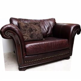 Leather Oversized Club Chair with Brass Tack Detail: An oversized leather club chair with brass tack detail. Featured is a brown leather chair with carved wood armrests and apron, rolled arms, brass rivet details, and bun feet. Includes accent pillow.