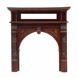 Victorian Style Carved Wood Fireplace Mantel: A Victorian style carved wood fireplace mantel in a mahogany finish. The mantel features a molded top shelf with turned wood supports and a rectangular beveled glass mirror. The arched fireplace opening has carved detailing with an applied carved wood accent to the center. Unmarked.