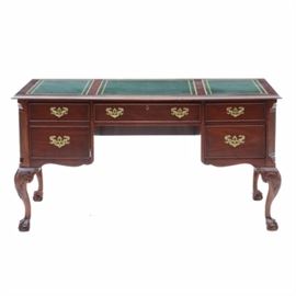 Leather Top Mahogany Desk: A traditional style office desk in mahogany, with a dark green leather, veneered top. It features three leather panels with gold-tone foliate borders, five drawers with hanging brass pulls and dovetail joints, and cabriole legs with carved knees and claw-and-ball feet. Unmarked.