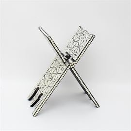 Vintage Qu'ran Stand with Mother of Pearl Inlay: A vintage Qu’ran stand with mother of pearl inlay. The Qur'an is the central religious text of Islam. This piece is constructed of wood and painted black. It is decorated with patterns of flowered running scrolls and mashrabiyya. It has no visible markings.