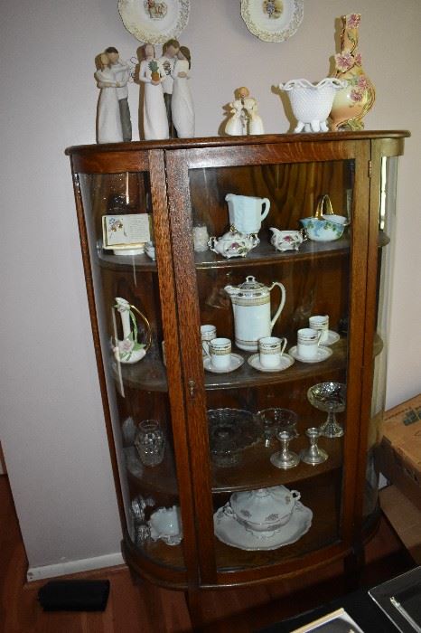 American Oak Curved Glass China Cabinet filled with Collectible items including Chocolate Set, Footed Case Glass Bowl with Fluted Edge, Willow Tree Figurines and more!