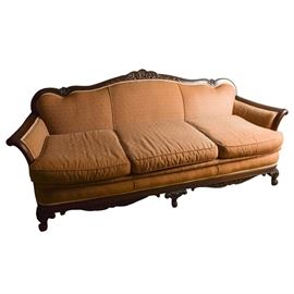 Victorian Walnut Camelback Sofa: A Victorian carved walnut camelback sofa with contemporary upholstery. The three-seat sofa features a carved serpentine crest, out-scrolled arms and carved front rail and legs. It has been fully reupholstered in warm tan fabric with pindot floral print and cream trim throughout. Sofa matches armchair listed separately as item 17CIN384-044.