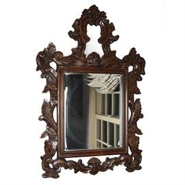 Vintage Carved Wood Wall Mirror: A vintage carved wall mirror. The frame is made from lightweight stained hardwood planks with Baroque-inspired swag and foliate carvings. Surrounds a center rectangular beveled glass mirror, ready to hang.