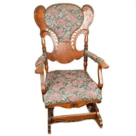 Antique Platform Rocking Chair: An antique platform rocker. This Victorian quarter sawn oak rocker has a stylized carved balloon back, curved arms, scalloped carved apron and spring-rocker base with floral tapestry and brass tack trim to the headrest, arms and seat.