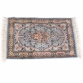 Pakistan Wool Hand Woven Blue and Brown Floral Area Rug: A Persian style hand woven small area rug from Pakistan. This piece has a central tan ellipsis with floral design inside, on a blue field with pink, cream, tan, and black floral design. It has an inner border with scalloped edges and scrolled accents to each side of medallions in each corner. The wide border has a floral detail comparable to the central medallion. It has overcast borders and off-white fringe to the narrow ends.