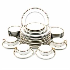 Tressemanes & Vogt Limoges Service C. 1895- 1917: A partial thirty-eight piece dinner service of Tressemanes & Vogt porcelain from the Limoges region of France. The pieces are decorated with green scrolls and rosettes around the border with a gilded rim. The collection contains twelve dinner plates, ten salad plates, eight fruit bowls, and two bread plates. Also included are four tea cups and saucers. There are printed factory marks dating the pieces to between 1895- 1917 consisting of a bell in puce reading “Limoges T.V No 6439”.