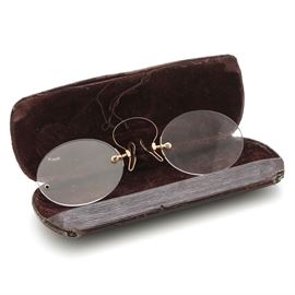 Pince-nez Spectacles with 10K Yellow Gold Spring Bridge and Carrying Case: A pair of Pince-nez glass rimless spectacles with 10K yellow gold spring bridge and brown carrying case with velvet interior. This style of glasses, popular in the 19th century, are supported without earpieces, by pinching the bridge of the nose. The name comes from French pincer, “to pinch”, and nez, “nose”.