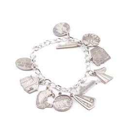 Kentucky Themed Sterling Silver Charm Bracelet: A Kentucky themed sterling silver charm bracelet. The link style bracelet includes eleven various charms and has a spring ring clasp. Some of the charms include a fish, a Cumberland Falls waterfall scene, a Kentucky state shape charm, among other Kentucky themed charms. The total weight, inclusive of all materials, is 1.255 ozt.