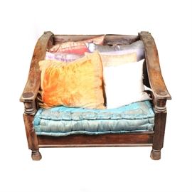 Tibetan-Style Chair: A Tibetan-style chair. This wooden chair features a slatted back, seat, and sides with sloping arms and turned arm supports. It rests upon bun feet and includes a rectangular blue seat cushion with a floral border. Six throw pillows in shades of pink, gold, purple, and white are included. See matching items 17LAX108-003, 17LAX108-004, and 17LAX108-007.