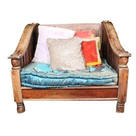 Tibetan-Style Chair: A Tibetan-style chair. This wooden chair features a slatted back, seat, and sides with sloping arms and turned arm supports. It rests upon bun feet and includes a rectangular blue seat cushion with a floral border. Four throw pillows in shades of red, gold, purple, and white are included. See matching items 17LAX108-002, 17LAX108-003, and 17LAX108-007.