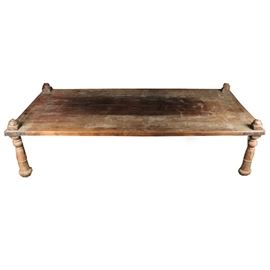 Tibetan-Style Coffee Table: A Tibetan-style wooden coffee table. This rectangular table rests upon four turned legs and is embellished with metal accents to each corner. The legs have traces of red paint.