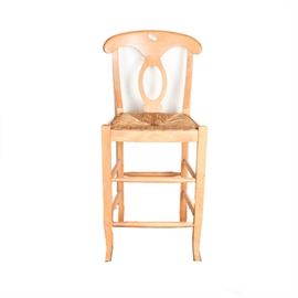Maple Bar Stool: A maple bar stool. This chair features a curved crest rail with fiddleback and a wicker seat with side aprons rises on splayed legs joined by stretchers. There are no visible maker’s marks or labels on this piece.