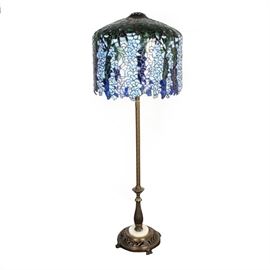 Tiffany Style Stained Glass Floor Lamp: A stained glass Tiffany style floor lamp. This lamp features a circular pierced brass base with a floral motif and scrolled feet. The top features a multi-piece domed blue, white, and green stained glass shade with a hanging blue foliate design.