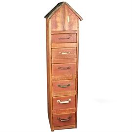 Repurposed Wood Birdhouse Style Cabinet: A repurposed wood birdhouse style cabinet. This piece features a top with two slanted sides opening on one side above six stacked drawers with various styles of pull handles terminating on a plinth base. There are no visible maker’s marks or labels on this piece.