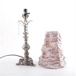 Silver Tone Table Lamp: A silver tone ornate table lamp. This footed ornate lamp has a bulbous piece at the base of the stem with curved arms at the top decorated with strands of clear hexagon shaped beads. The lamp includes a pink ruffled cloth shade.