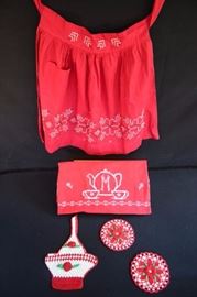 Vintage Red Hostess Collection: Tablecloth 34" x 48" monogrammed with an "M", decorated with hand cross-stitching and embroidery piped with white bias tape, 2 red and white round hand crocheted  potholders with red flowers 6", red and white basket potholder with red flowers and red apron decorated with white and black cross stitching. This lot is in very good condition and shows little wear, if any - no rips, stains or holes