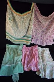 Assorted Vintage Handmade Aprons: Pink & White gingham with 1 pocket and hand-stitched border, Mint Green with 1 pocket and trimmed with white, Mint Green, pink & Yellow flower bouquets on off-white background, no pocket (rust stains on waistband), Lime Green, Rose Pink and Lavender paisley print on pink background etched with white rick-rack with 1 pocket, Yellow Blue & Green mini-flowers on white background trimmed with Green, blue, yellow red and orange striped fabric.  Other than one mentioned above, all are in very good vintage condition.