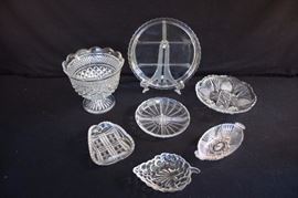 8-Piece Clear Glass Collection: pressed glass large pedestal bowl 7" high, 7" diameter; small oval serving dish with handles (1 is chipped) (8.5" x 4");  8.25" round serving dish with 4 sections and scalloped edges; 9" footed pressed glass serving dish with scalloped edges; 10.5 round serving dish with 4 sections and scalloped edges; 7" x 4.5" "bunch of grapes" small serving dish; 6" x 5.25 small pressed glass irregular-shaped serving dish with scalloped edges. This lot is in very good condition and shows little wear, if any - no chips or cracks